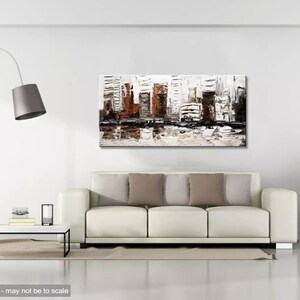 May include: Abstract painting of a city skyline in shades of brown, gray, and white. The painting is displayed on a white wall above a white sofa with brown pillows.