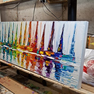 May include: A colorful abstract painting of sailboats on a white background. The painting is done in a thick impasto style, with visible brushstrokes. The sailboats are painted in a variety of bright colors, including red, orange, yellow, green, blue, and purple. The water is painted in a lighter blue and white, with hints of green and yellow. The painting is framed in a white frame.
