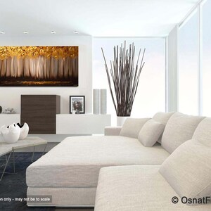 May include: Abstract painting of a forest with gold and brown tones. The painting is hanging on a white wall in a modern living room with a white couch and pillows.