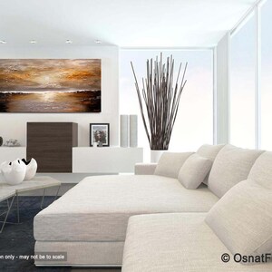 May include: Abstract painting of a sunset over a body of water. The painting is in shades of brown, gold, and white. It is displayed on a white wall in a modern living room setting.