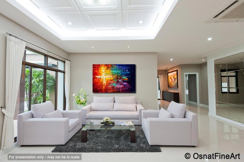 May include: Abstract painting with a cross shape in the center, featuring vibrant colors like red, orange, yellow, green, blue, and purple. The painting is displayed on a wall in a living room setting with white furniture.