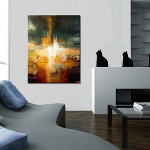 May include: Abstract painting with a mix of warm and cool colours, featuring a central white shape surrounded by shades of orange, yellow, brown, and green. The painting is displayed on a white wall in a modern living room setting.