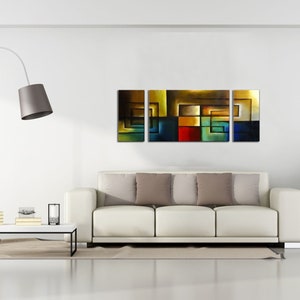 May include: Abstract art painting with a geometric design in shades of brown, blue, green, red, and yellow. The painting is divided into three panels and is displayed on a white wall above a white couch.