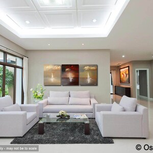 May include: A living room interior with three abstract paintings of sailboats on the wall. The paintings are in shades of gold, red, and blue. The room is furnished with a white sofa, two armchairs, and a coffee table. The floor is tiled in a light color.