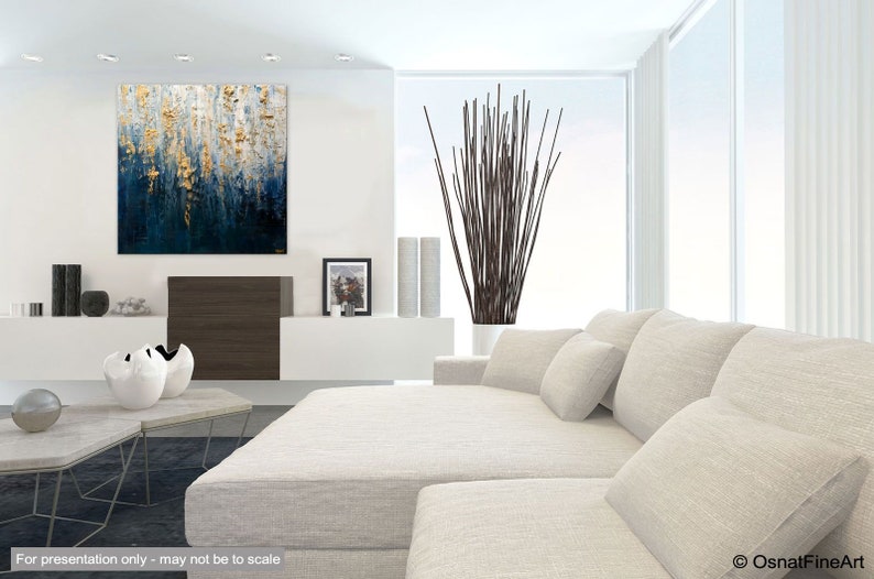 May include: Modern living room with a large abstract painting in shades of blue and gold. A white sectional sofa with several pillows is in the foreground. Decorative vases and a tall plant add to the contemporary design.