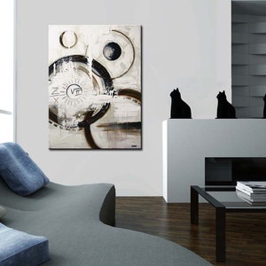 May include: Abstract painting with black and white circles and lines on a white background. The painting is framed and hanging on a white wall in a modern living room.
