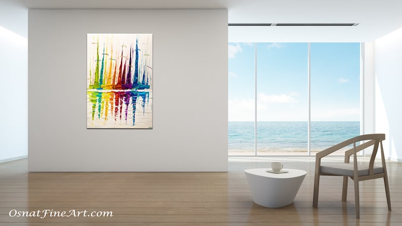 May include: Abstract painting of colorful sailboats reflected in the water. The painting is on a white canvas and is framed in a white frame. The painting is hanging on a white wall in a modern living room with a large window overlooking the ocean.
