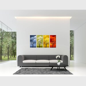 May include: Four framed canvas prints depicting a silhouette of a tree in different seasons. The prints are arranged in a row, with the first print showing the tree in winter, the second in spring, the third in summer, and the fourth in fall. The prints are hung on a white wall above a gray sofa.