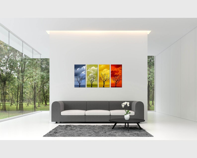 May include: Four framed canvas prints depicting a silhouette of a tree in different seasons. The prints are arranged in a row, with the first print showing the tree in winter, the second in spring, the third in summer, and the fourth in fall. The prints are hung on a white wall above a gray sofa.