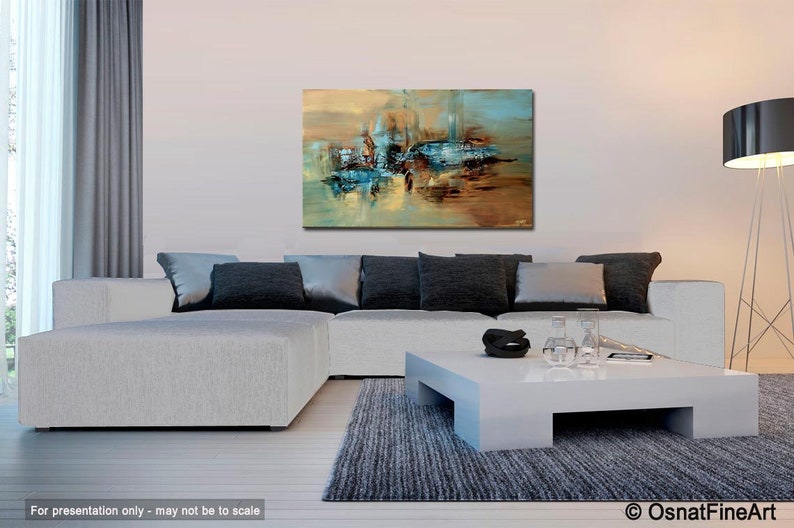 May include: Abstract painting with shades of blue, brown, and yellow. The painting is hanging on a white wall above a white sectional sofa with gray pillows. A white coffee table with a black bowl and clear glasses sits in front of the sofa.