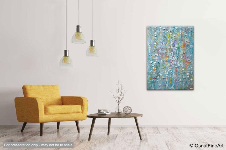 May include: Abstract painting with a textured surface in shades of blue, white, and yellow. The painting is hanging on a white wall in a living room setting with a yellow armchair and a coffee table.