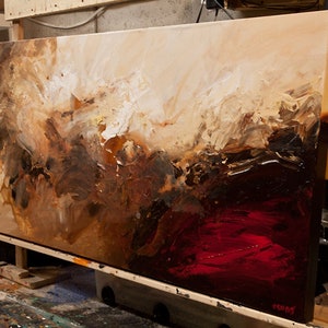 May include: Abstract painting on canvas with brown, white, and red paint. The painting is on an easel and is leaning against a wall.