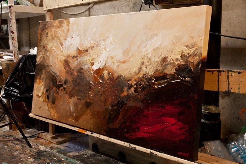 May include: Abstract painting on canvas with brown, white, and red paint. The painting is on an easel and is leaning against a wall.