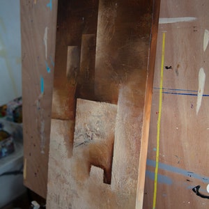 May include: A brown and beige abstract painting on canvas with a textured surface. The painting features geometric shapes and a layered effect.