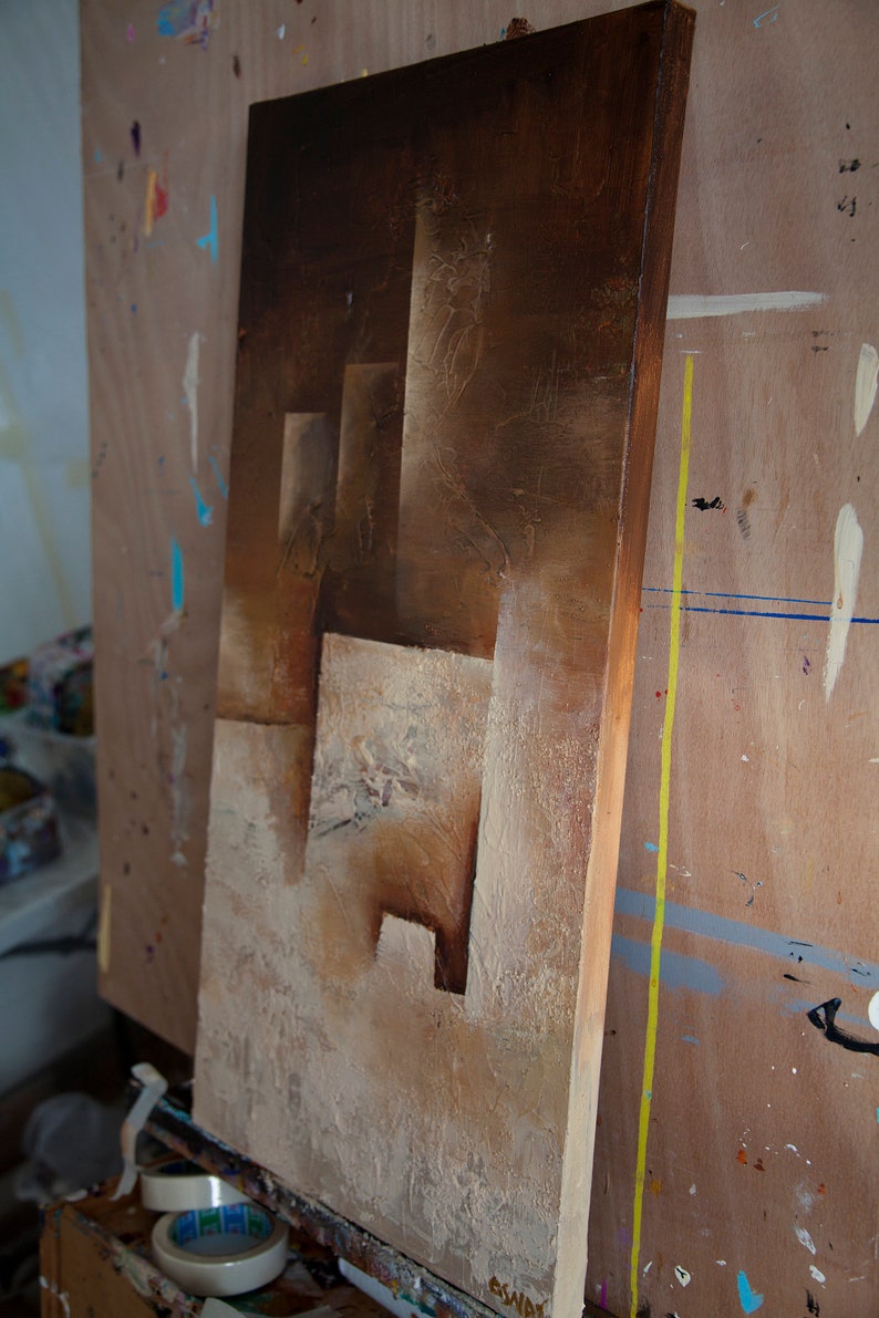 May include: A brown and beige abstract painting on canvas with a textured surface. The painting features geometric shapes and a layered effect.