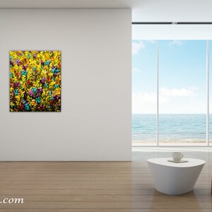 May include: Abstract painting of a field of yellow, blue, and purple flowers. The painting is displayed on a white wall in a modern living room with a view of the ocean.