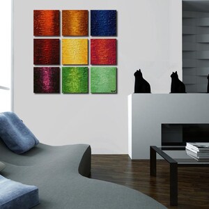May include: A nine-piece abstract painting set with colorful squares in shades of red, orange, yellow, green, blue, and purple. The paintings are arranged in a grid pattern on a white wall.
