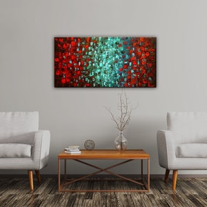 May include: Abstract painting with a red and teal color scheme. The painting is made up of small squares of color, creating a textured effect. The painting is hanging on a white wall in a living room setting.