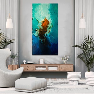 May include: Abstract painting with blue, green, and orange colors. The painting is hanging on a wall in a modern living room with a white armchair, a wooden coffee table, and two white plant stands with green plants.