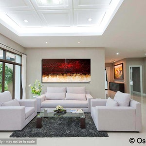 May include: Abstract painting with red, orange, and gold hues on a white canvas. The painting is hanging on a wall in a modern living room with white couches and a glass coffee table.