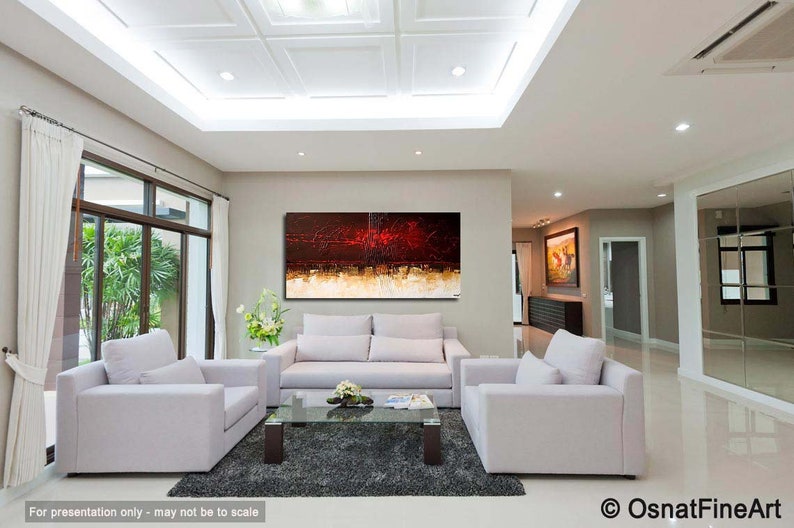 May include: Abstract painting with red, orange, and gold hues on a white canvas. The painting is hanging on a wall in a modern living room with white couches and a glass coffee table.