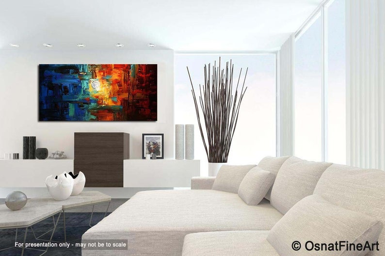 May include: Abstract painting with a mix of blue, green, orange, and red colors. The painting is displayed on a white wall above a white couch with pillows.