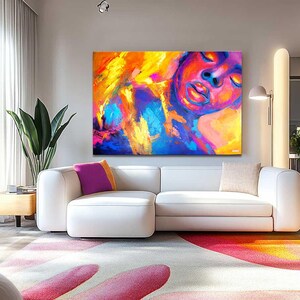 May include: A modern living room featuring a large abstract painting with vibrant colors of yellow, orange, blue, and purple. A white sectional sofa with colorful throw pillows sits below the artwork. The room has large windows and a patterned rug.
