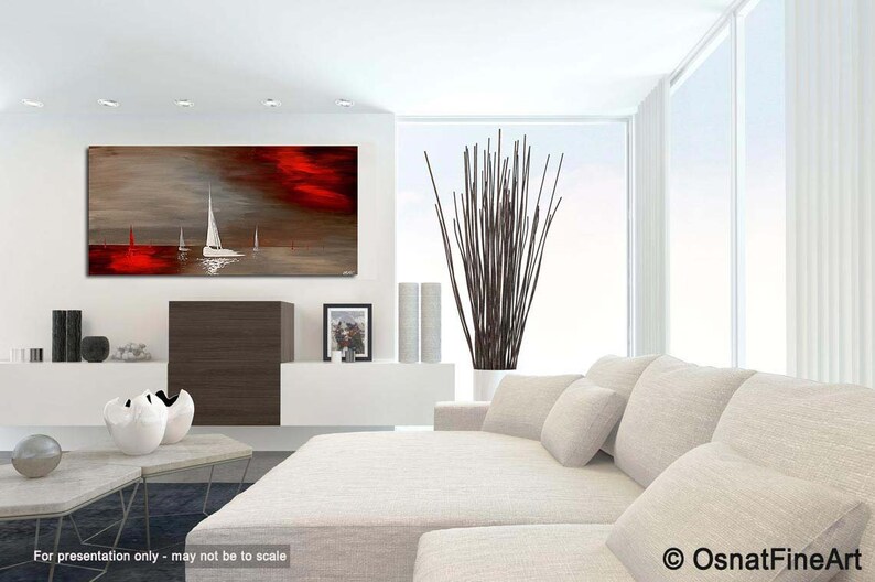 May include: Abstract painting of sailboats on a red and gray water scene. The painting is hanging on a white wall in a modern living room with a white couch and a vase of brown branches.