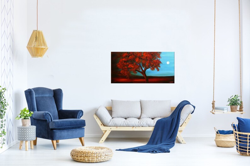 May include: A painting of a lone tree with red leaves against a blue sky with a full moon. The tree is in the foreground and the moon is in the background. The painting is framed and hanging on a white wall.