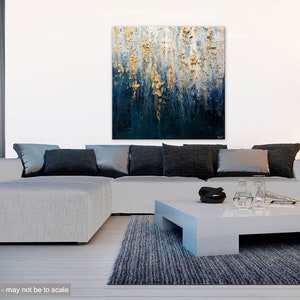 May include: Abstract wall art featuring a textured painting with gold and blue tones. The artwork hangs above a light gray sectional sofa with dark gray and silver pillows. A white coffee table and a gray rug complete the living room setting.