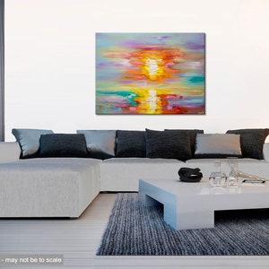 May include: Abstract painting of a colorful sunset over a body of water. The painting is done in shades of pink, orange, yellow, green, and blue. The painting is displayed on a white wall above a gray couch and a white coffee table.