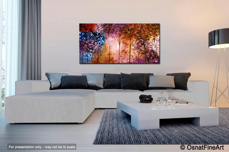 May include: Abstract painting of a forest scene with colorful trees in shades of purple, orange, red, and blue. The painting is displayed on a white wall above a white sectional sofa with gray throw pillows.