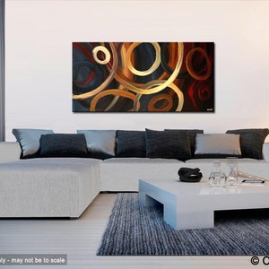 May include: Abstract painting with a black background and overlapping circles in shades of gold, brown, and red. The painting is displayed on a wall in a living room setting with a white couch and a coffee table.