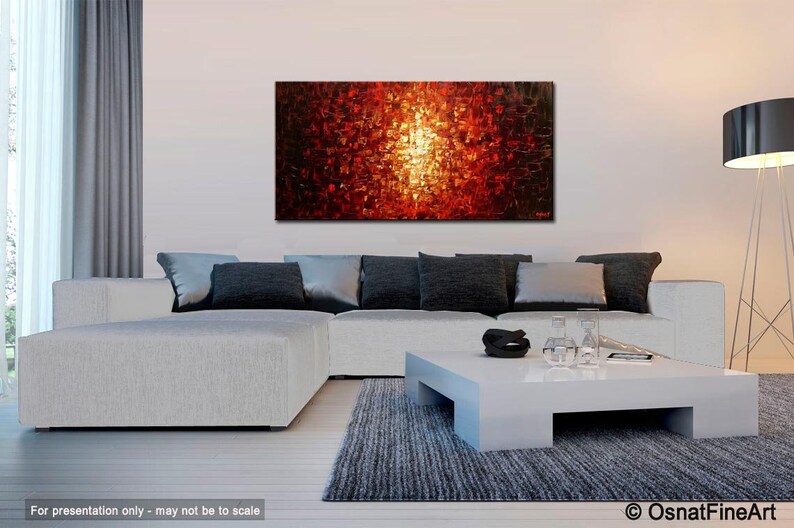 May include: Abstract painting with a bright yellow center surrounded by red, orange, and black squares. The painting is hanging on a white wall above a white sectional sofa with gray pillows. A white coffee table with a black bowl and clear glasses sits in front of the sofa.