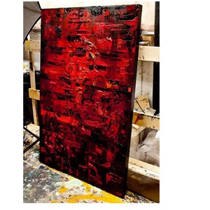 May include: Abstract painting with a textured surface. The painting is dominated by shades of red and black, with hints of orange and yellow. The paint is applied in thick layers, creating a sense of depth and movement.