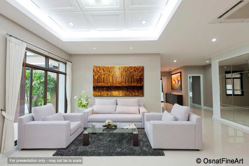 May include: A large abstract painting of a forest scene with golden and brown hues. The painting is hanging on a wall in a living room with white furniture and a glass coffee table.