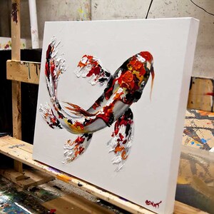May include: A white canvas painting of a koi fish with red, orange, black, and white scales. The fish is painted in a textured style, giving it a three-dimensional appearance.