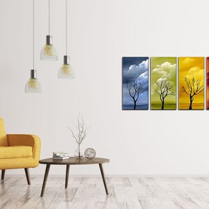 May include: A set of four abstract paintings depicting a bare tree in different seasons. The paintings are in shades of blue, green, yellow, and orange, with clouds in the sky. The paintings are hung on a white wall in a living room setting.