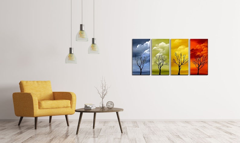 May include: A set of four abstract paintings depicting a bare tree in different seasons. The paintings are in shades of blue, green, yellow, and orange, with clouds in the sky. The paintings are hung on a white wall in a living room setting.