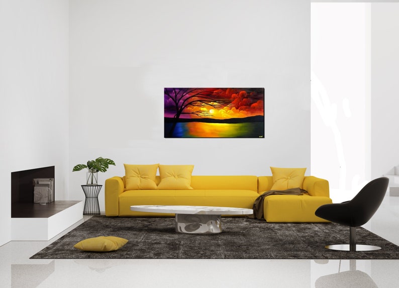 May include: A painting of a sunset over a lake with a silhouetted tree in the foreground. The sky is a vibrant mix of purple, orange, and red. The painting is framed and hanging on a white wall above a yellow sofa.