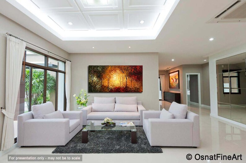 May include: A living room interior with a large abstract painting of a forest scene in shades of orange, yellow, and green. The painting is hanging on a wall above a white sofa. There are two white armchairs in front of the sofa and a glass coffee table in the center of the room.