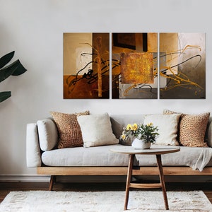 May include: A three-piece abstract art print set with brown, gold, and gray colors. The artwork features geometric shapes and lines, creating a modern and stylish design.