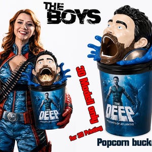 Op de afbeelding: Een popcornemmer en een drinkbeker met "The Deep" uit "The Boys". De emmer heeft een 3D-hoofdontwerp met blauwe waterspetterdetails. De beker en de emmer hebben de tekst "The Deep" en "Thoughts of Atlantis".