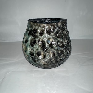 Könnte beinhalten: Eine handgefertigte Keramikvase mit strukturierter, blasenartiger Oberfläche. Die Vase hat eine Farbpalette aus Schwarz, Grau und Blaugrün mit einem dunklen Rand. Das einzigartige Design verleiht der Vase ein unverwechselbares, organisches Aussehen, geeignet für die Inneneinrichtung.