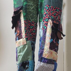 May include: Patchwork pants featuring a variety of fabric squares in shades of green, blue, purple, and red with floral, paisley, and geometric patterns. The pants have an elastic waistband and two large cargo-style pockets on the outer thighs.