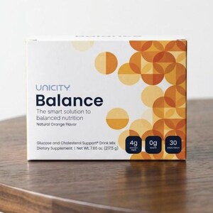 K&ouml;nnte beinhalten: Eine wei&szlig;e Schachtel mit Unicity Balance-Getr&auml;nkemix mit orangefarbenen und gelben geometrischen Designs. Auf der Schachtel steht "Balance" und "Die intelligente L&ouml;sung f&uuml;r ausgewogene Ern&auml;hrung". Die Schachtel steht auf einem Holztisch.