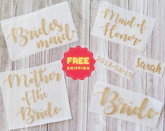 May include: A collection of gold glitter iron-on decals on white backing paper. The text includes Bridesmaid, Maid of Honor, Mother of the Bride, Bride, Sarah, and the date 2018-08-19, all written in a cursive script font style.