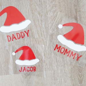 May include: Three red and white Santa hat iron-on transfers with the names "Daddy", "Mommy", and "Jacob" printed below each hat.