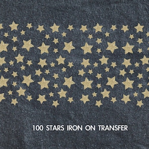 May include: A sheet of 100 gold glitter iron-on stars on a dark blue denim background.  The text "100 STARS IRON ON TRANSFER" is printed below the stars.
