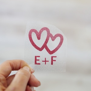 May include: A clear sticker with two red intertwined hearts and the text "E+F" in red.
